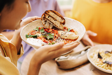 Woman holding bowl of shakshuka with friends at restaurant