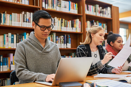 Laptop, typing and man in library for study with university, education and scholarship for growth. Books, online research and college student on campus with learning, knowledge and writing paper