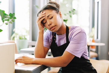 Tired african american waitress suffering headache sitting at table in cafe