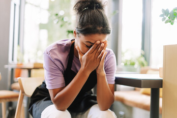 Young, unhappy African American tired waitress covering her face with hands in a restaurant
