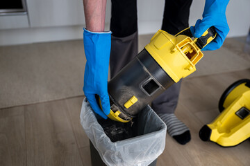 Close-up of hands in blue gloves emptying garbage into a bucket from a container and a vacuum cleaner filter.