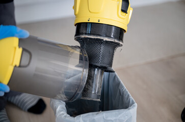 Close-up of a man's hands in blue gloves holding a vacuum cleaner filter over a trash can