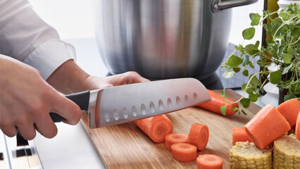 Closeup of a person dicing carrots on a wooden cutting board.