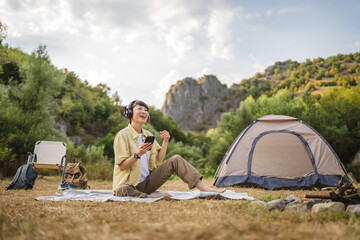 Japanese woman sit in front a tent and listen to music on a cellphone