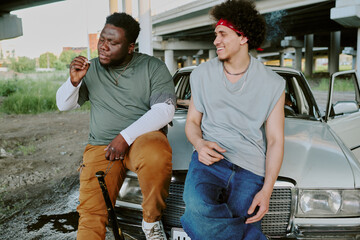 Biracial friends spending time together next to retro car while tough guy smoking