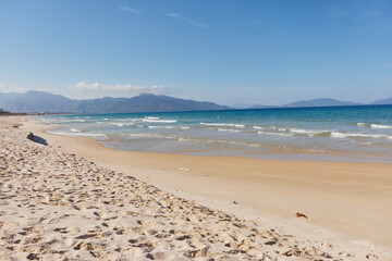 Sandy beach with crystal clear water, majestic mountains, and a vibrant blue sky in the background