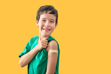 Studio portrait boy showing a plaster on his arm isolated against a yellow background. Cute...
