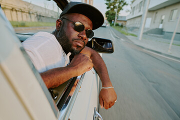 Young cool man with black sunglasses and black cap looking out of car window