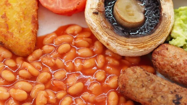 A plate of vegetarian breakfast with baked beans, toast, hash brown, grilled tomato, mushroom, and avo