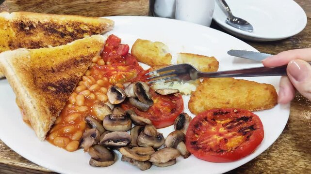 A plate of vegetarian breakfast with baked beans, toast, hash brown, grilled tomato, mushroom, and avo