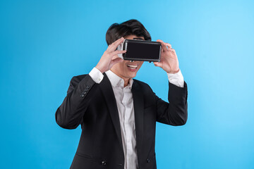 Smiling Asian businessman looking thorough VR connecting to business world report in futuristic metaverse, analyzing innovation technology ads in virtual reality isolated blue copyspace. Contrivance.