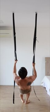 homem em treino fisico  de costas com argolas penduradas 