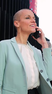 Vertical. Successful business woman with suit alking and talking by mobile phone. Businesswoman having a call conversation on a cellphone. Executive female chatting using a smartphone at workplace.