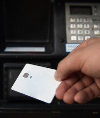 Hand holding a contactless card near a card scanner at a payment terminal in a city. A hand is poised to tap a contactless banking card against a payment terminal.