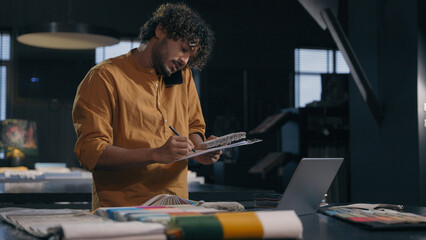 Indian business man arabian businessman decorator male tailor fashion designer couturier multitasking work talking mobile phone with client writing notes online order sample fabrics in cloth atelier