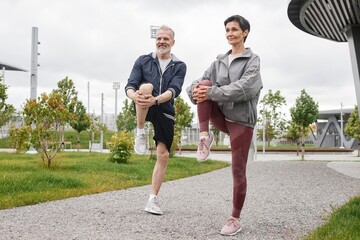 Full shot of smiling senior man and woman doing standing knee hugs, warming up and getting ready to...