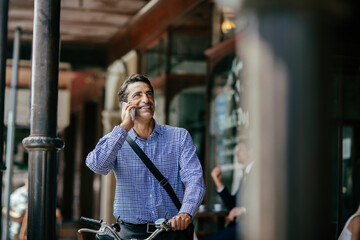 Middle aged businessman with smartphone commuting in city with bike