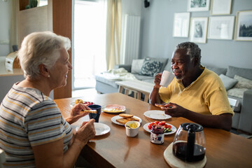 Diverse senior couple eating breakfast together on the kitchen table
