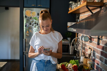 Smiling young woman using smartphone in modern kitchen