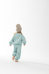 Fototapeta premium Portrait of beautiful cute little toddler girl. Child with funny face in mint sweatshirt and hat. Pretty smile kid in studio on white background.