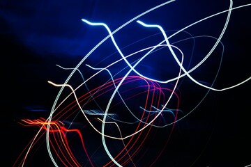 The image is a colorful abstract of light and dark lines. The colors are red, blue, and white, and the lines are wavy and curvy. Scene is energetic and dynamic, with the lines