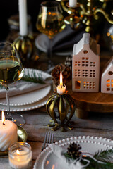 Beautiful table setting for family Christmas dinner at home. Cozy atmosphere, candlelight. Wine glasses, vintage chandelier, elegant interior. Fir tree branches, wooden furniture, dark, bokeh