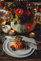 Cozy festive holiday table decor for home family Thanksgiving dinner. Traditional event, elegant natural decoration. Wooden rustic table, countryside style. Burning candles, floral centrepiece pumpkin