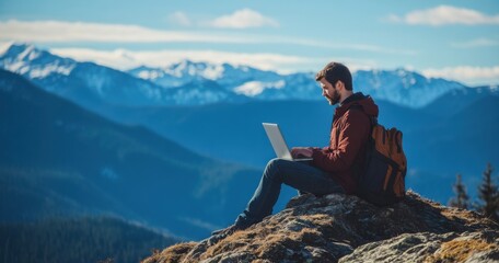 A young man works on a laptop while sitting at the top of a mountain. This concept represents the digital nomad lifestyle and the ability to work remotely or travel using the internet.