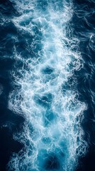 A long, white streak of foamy water cuts through the deep blue ocean, creating a mesmerizing pattern.