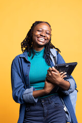 Portrait of smiling BIPOC woman holding laptop, preparing to start work shift, isolated over studio background. Grinning worker with notebook ready to do business related tasks on it