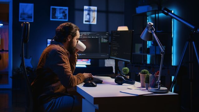 Computer scientist drinking cup of coffee while developing code on PC using java programming languages. IT admin brainstorming ways of fixing database errors, enjoying hot beverage, camera B