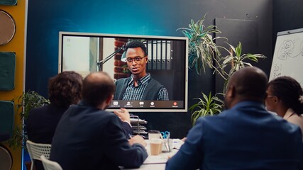 Team attends meeting with the business administrator to present a project briefing, addressing annual data reports and performance metrics via videocall conference online. Camera B.