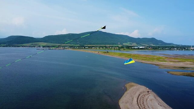 Un Cerf-volant en vol stationnaire sous un ciel bleu avec en arri&egrave;re-plan un d&eacute;cor marin pittoresque form&eacute; de montagnes, banc de sable & village lointain. ( Carleton-sur-mer, Gasp&eacute;sie,Qu&eacute;bec, Canada.)