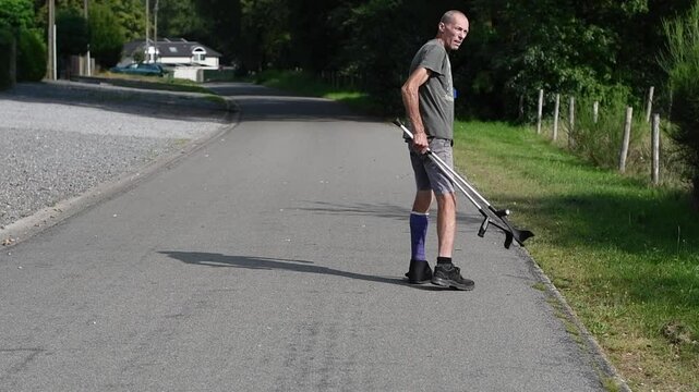man with broken left leg in modern blue fiberglass plaster cast with walking shoes, walking with crutches, keeping injured leg up, protecting from stress, rehabilitation concept,