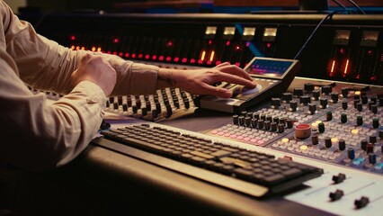 Audio technician uses mixing console and faders in control room, remote control for adjusting sound...