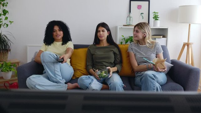 Three happy college female students working together on laptop at home. Millennial student flatmate friends enjoying time together at shared apartment.