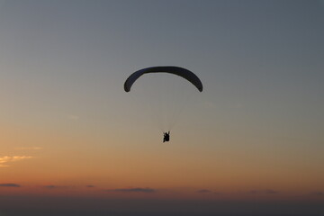 Paraglider silhouette gliding over clouds and sunset in California