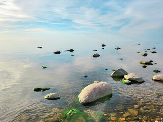  Calm waters and scattered rocks with moss under a soft morning sky. Perfect for themes of nature’s tranquility and coastal beauty.