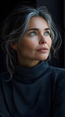 Fototapeta premium A woman with grey hair looks thoughtfully off-camera, her blue eyes are striking against her dark sweater.