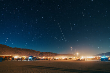 Fototapeta premium Celestial Wonder: Shooting Stars Above a Desert Festival