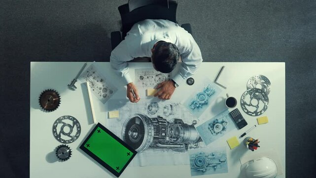 Top down view of skilled engineer writing and planning turbine engine design while sitting at meeting table with gear and electronic generator scatter around. Technician taking a note. Alimentation.