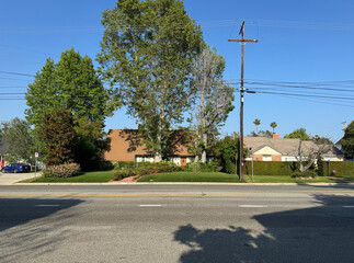 empty residential street (homes, front lawns, trees, sidewalk, road, telephone pole and utility wires, parked cars) beneath a bright blue summer sky - typical generic American suburb - Los Angeles