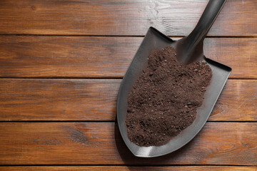 Metal shovel with soil on wooden table, top view. Space for text