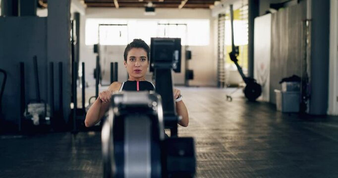Fitness, woman and rowing machine in gym for training, workout or cardiovascular exercise. Strong athlete, serious challenge and row on sports equipment for energy, healthy muscle or power for action
