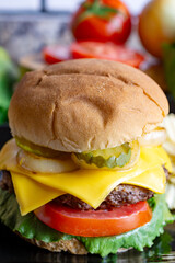 A cheeseburger on a black plate with pickles, fried onions, tomato an lettuce on a seedless bun.