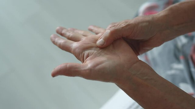 Dupuytren contracture and protuberance on palm. Elderly woman rubs, feels tender hand with stiff knot under ring finger. Senior female has trouble bending finger. Hand tendon malady, stiff knot.