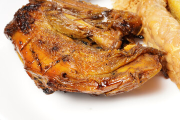 A plate of savory dishes including sweet grilled chicken with a dark brown color, fried tofu and tempeh, and crispy crumbs, served on a white plate against a dark background.