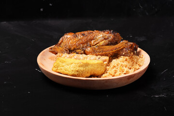 A plate of savory dishes including sweet grilled chicken with a dark brown color, fried tofu and tempeh, and crispy crumbs, served on a wooden plate against a dark background.