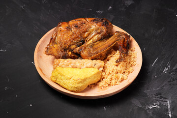A plate of savory dishes including sweet grilled chicken with a dark brown color, fried tofu and tempeh, and crispy crumbs, served on a wooden plate against a dark background.