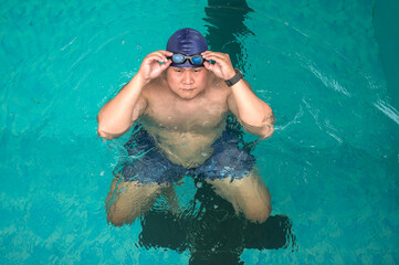 Fat Asian swimmer man adjust swim goggles during swimming in pool